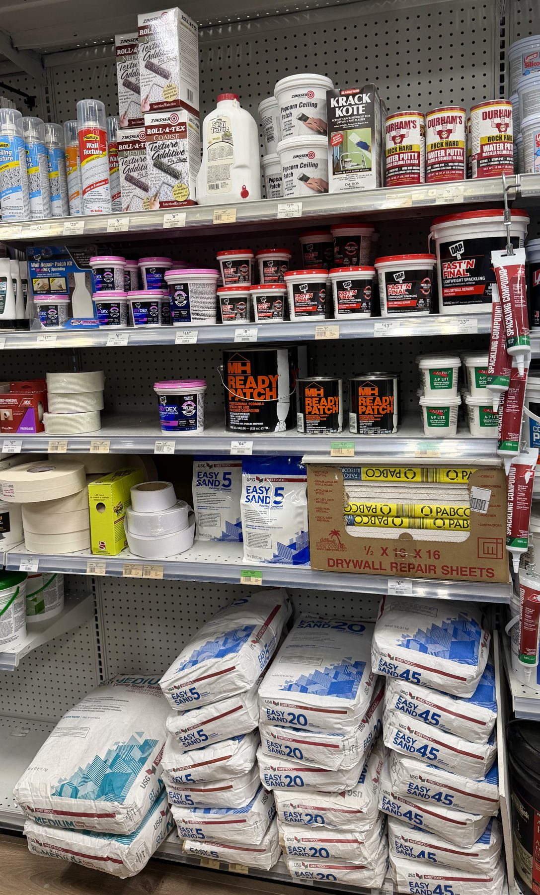 Shelves filled with drywall repair supplies including USG Sheetrock Easy Sand joint compound, DAP spackling, MH Ready Patch, and Durham's Rock Hard Water Putty at Hessler Paint & Hardware in Delray Beach, Florida.