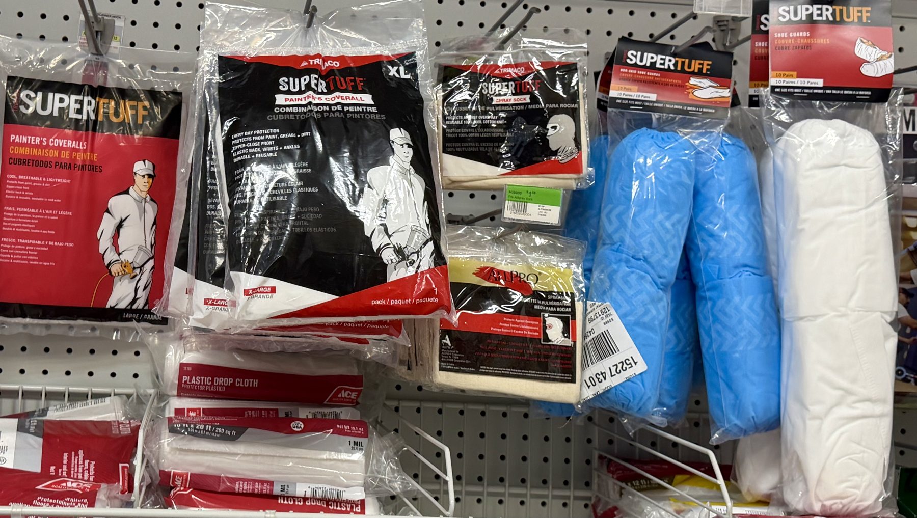 Trimaco SuperTuff painter's coveralls, spray socks, shoe guards, and Ace plastic drop cloths on display hooks at Hessler Paint & Hardware in Delray Beach, Florida.
