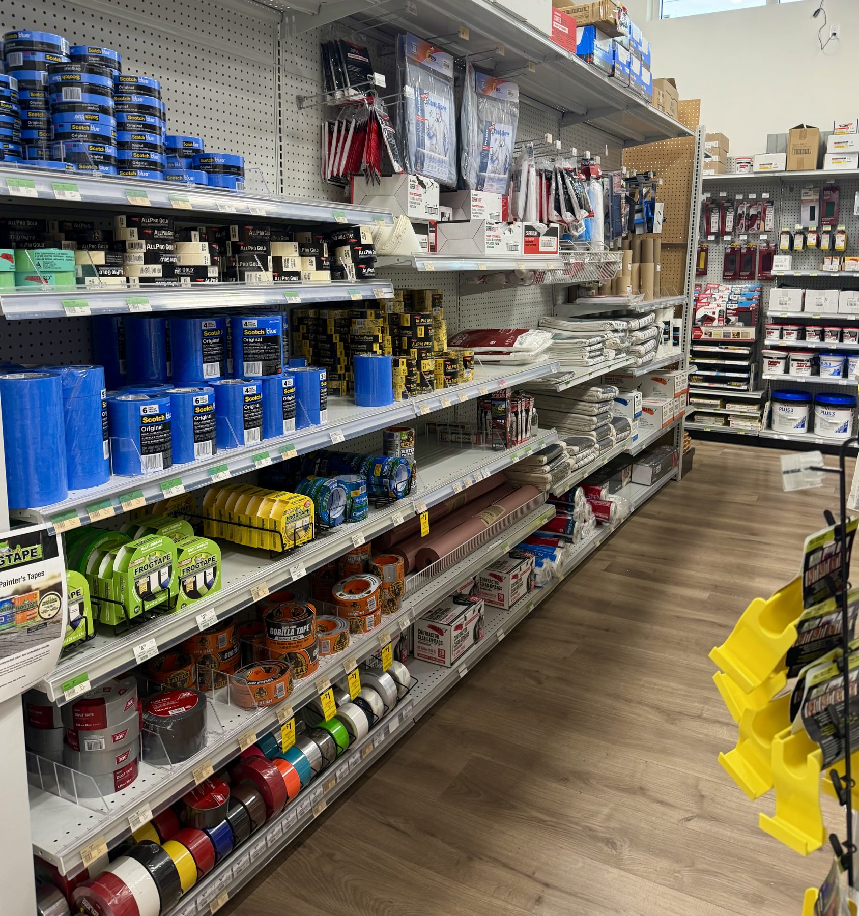 Aisle shelves fully stocked with ScotchBlue painter's tape, FrogTape, Gorilla tape, masking tapes, and plastic drop cloths at Hessler Paint & Hardware in Delray Beach, Florida.