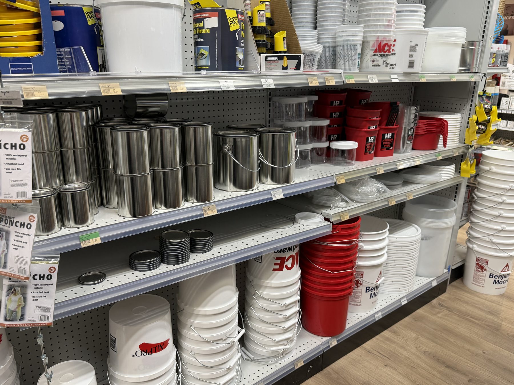 Shelves stocked with empty metal paint cans, plastic paint mixing containers, Handy Paint Pails, and stacks of Ace Hardware, ALLPRO, and Benjamin Moore paint buckets at Hessler Paint & Hardware in Delray Beach, Florida.