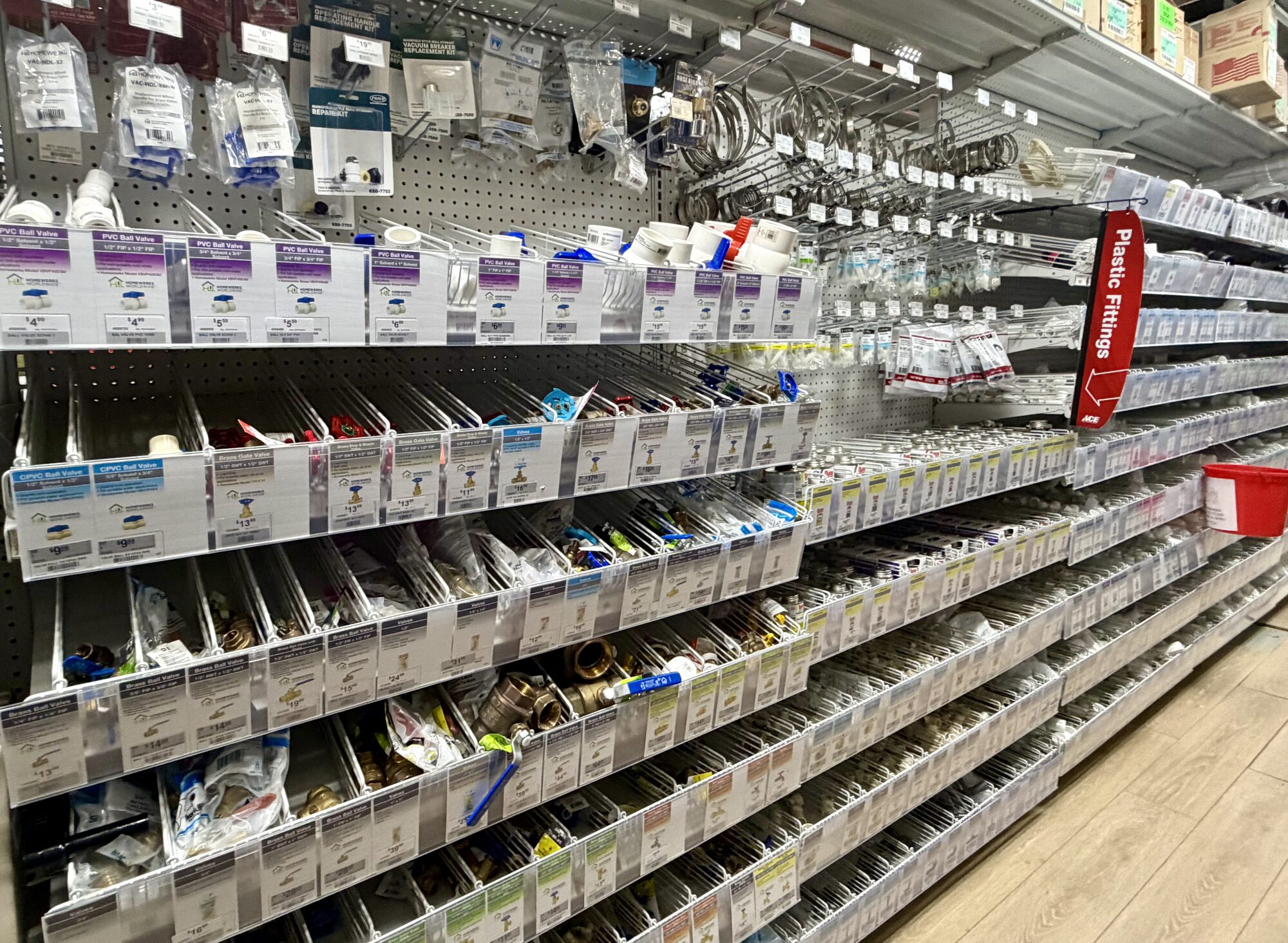 Shelves stocked with Ace branded PVC ball valves, plastic fittings, and assorted plumbing hardware at Hessler Paint & Hardware in Delray Beach, Florida.