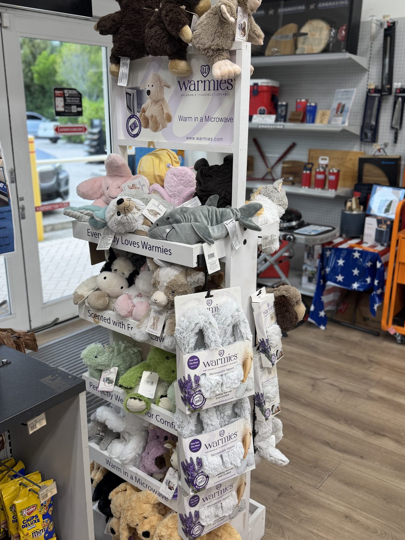 Warmies display rack featuring microwavable stuffed plush animals, lavender-scented plushies, and cozy slippers at Hessler Paint & Hardware in Delray Beach, Florida.