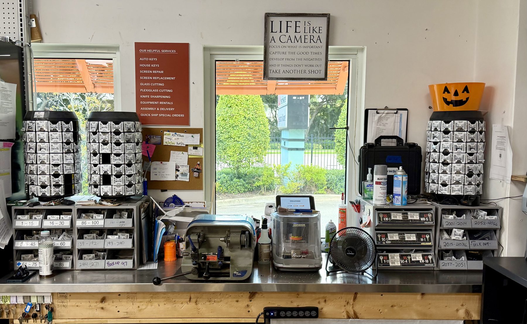 Key cutting and duplication bench with key blank carousels, key blanks drawers, key duplication machines, and helpful services sign at Hessler Paint & Hardware in Delray Beach, Florida.