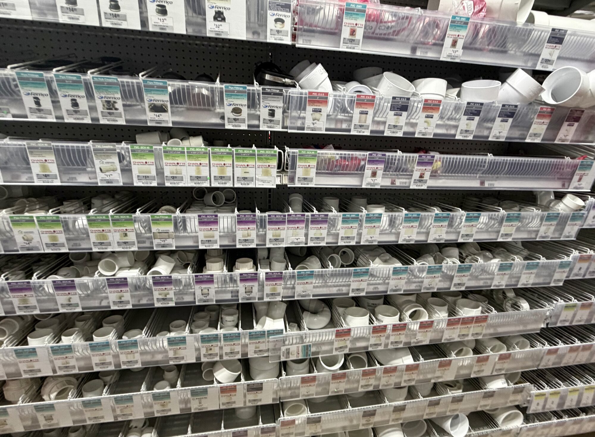Shelves stocked with various white PVC pipe fittings and Fernco couplers at Hessler Paint & Hardware in Delray Beach, Florida.