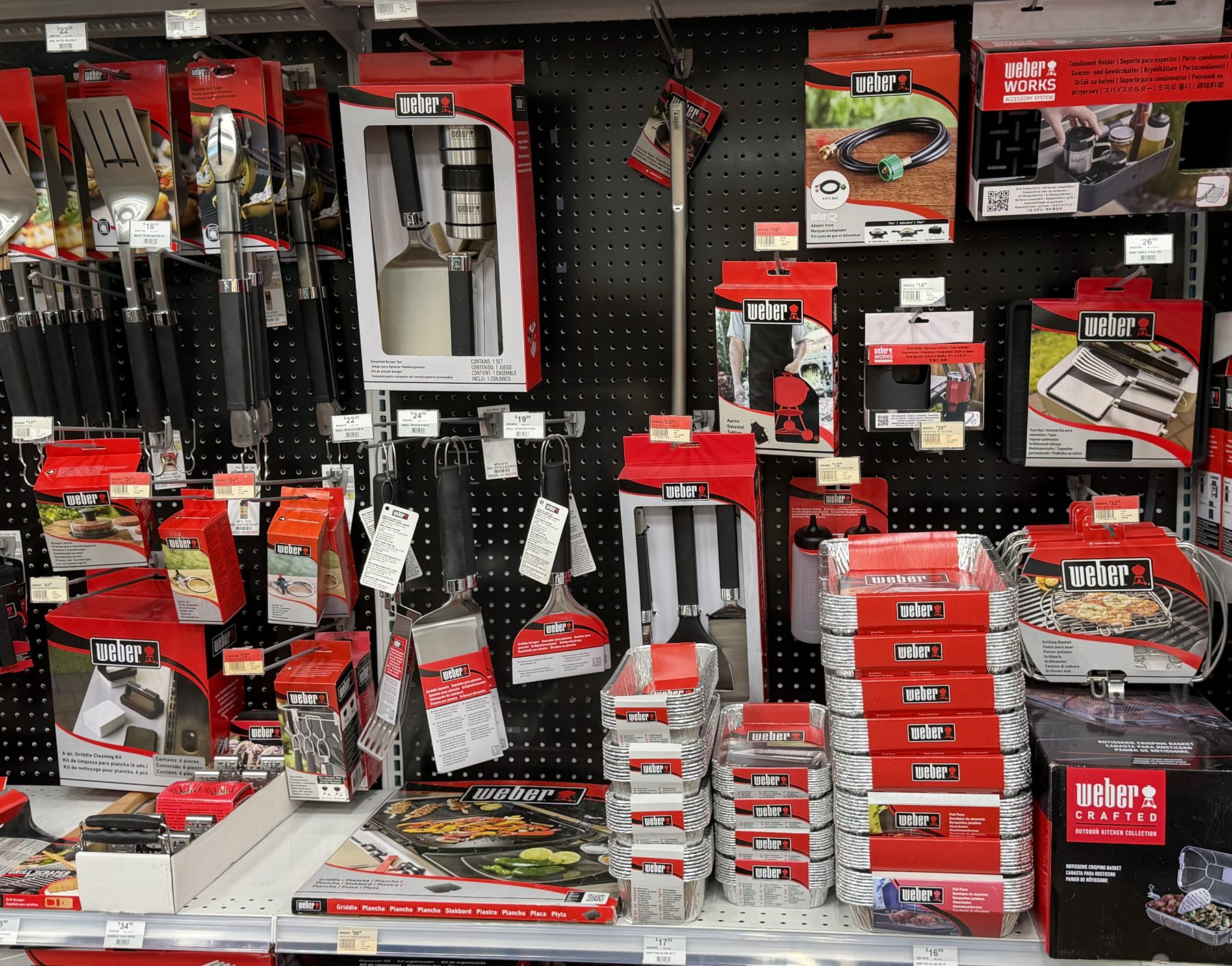 A wide selection of Weber grilling tools, spatulas, tongs, and disposable aluminum drip pans on display at Hessler Paint & Hardware in Delray Beach, Florida.