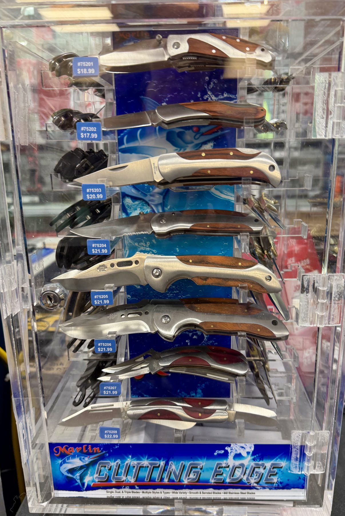 A clear acrylic display case featuring Marlin Cutting Edge folding pocket knives with wood grain and stainless steel handles at Hessler Paint & Hardware in Delray Beach, Florida.