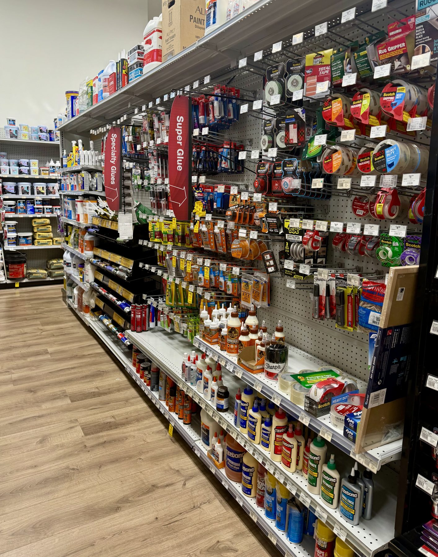 Store aisle displaying Scotch packaging tapes, Titebond wood glues, Gorilla Glue, and specialty adhesives at Hessler Paint & Hardware in Delray Beach, Florida.