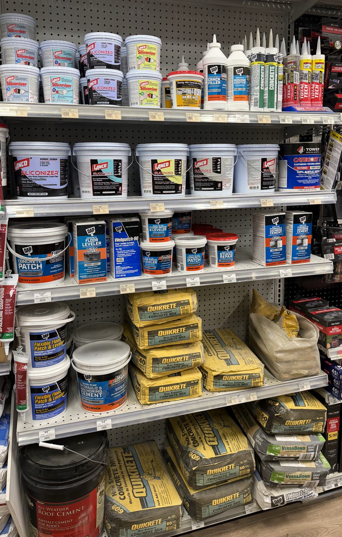 Shelves stocked with Lanco Siliconizer, DAP Concrete Patch, DAP floor leveler, and Quikrete concrete mix bags at Hessler Paint & Hardware in Delray Beach, Florida.