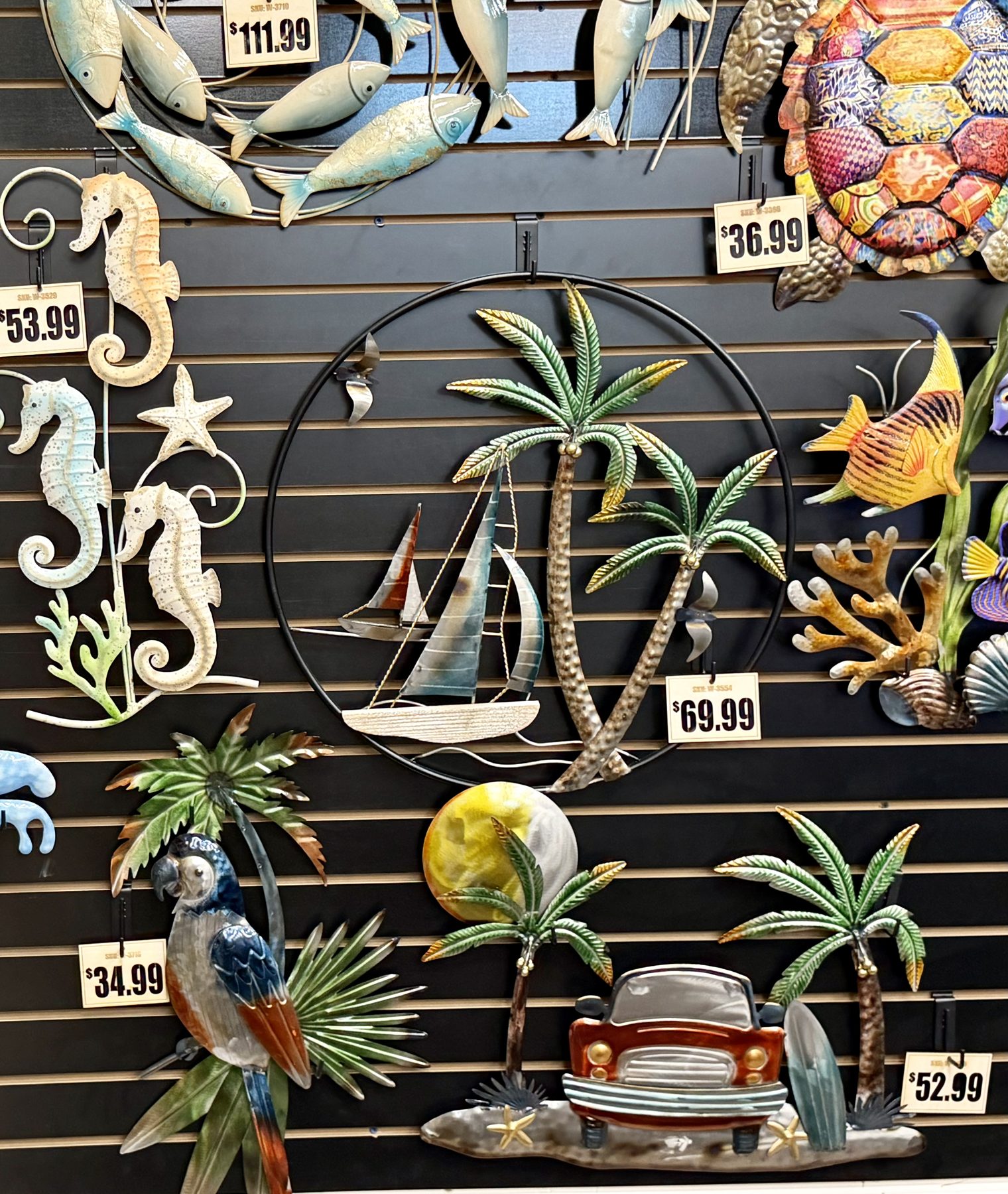 Vibrant coastal metal wall art display featuring palm tree sailboat sculptures, seahorses, colorful sea turtles, parrots, and beach decor at Hessler Paint & Hardware in Delray Beach, Florida.