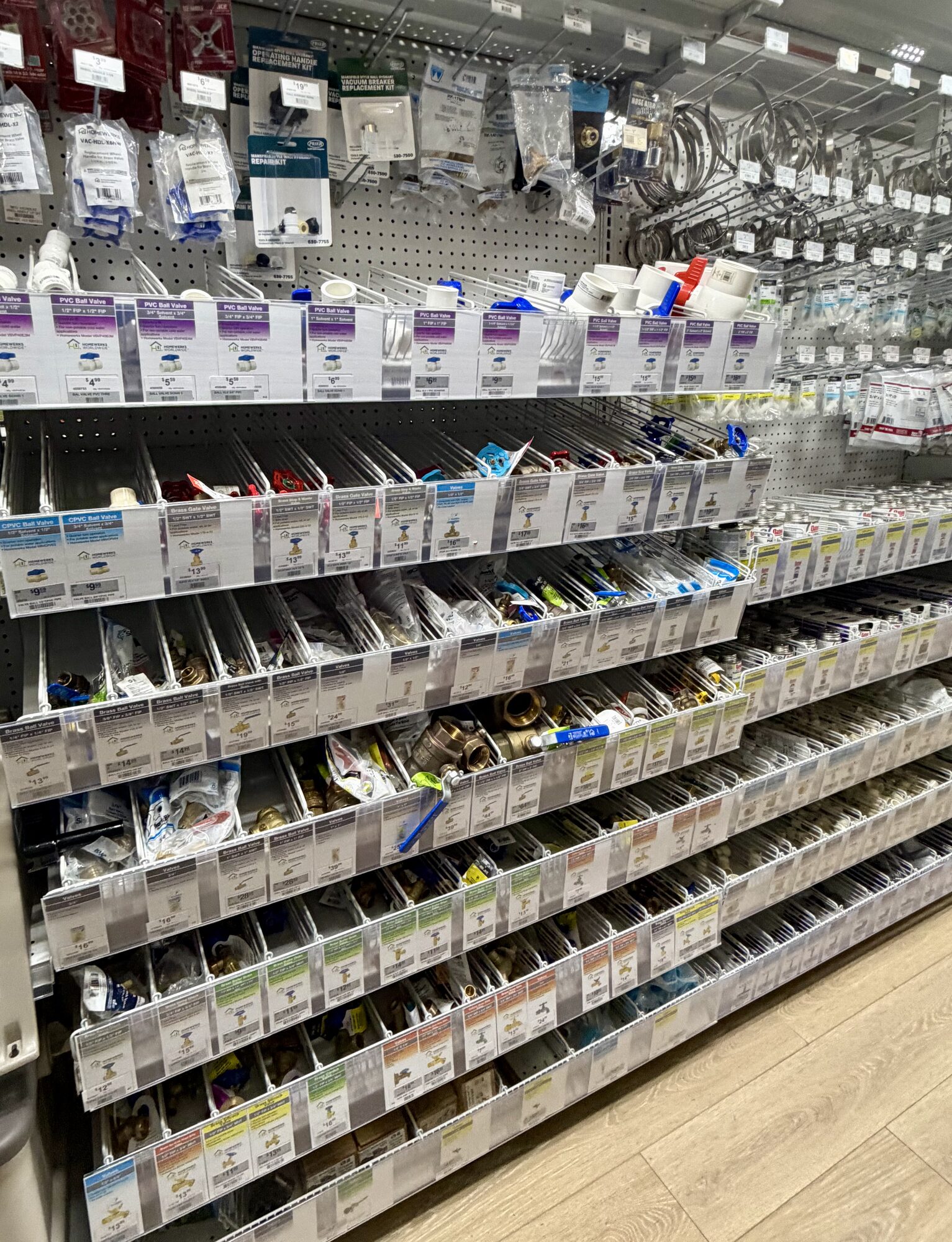 Shelves stocked with PVC ball valves, brass fittings, and plumbing repair kits at Hessler Paint & Hardware in Delray Beach, Florida.