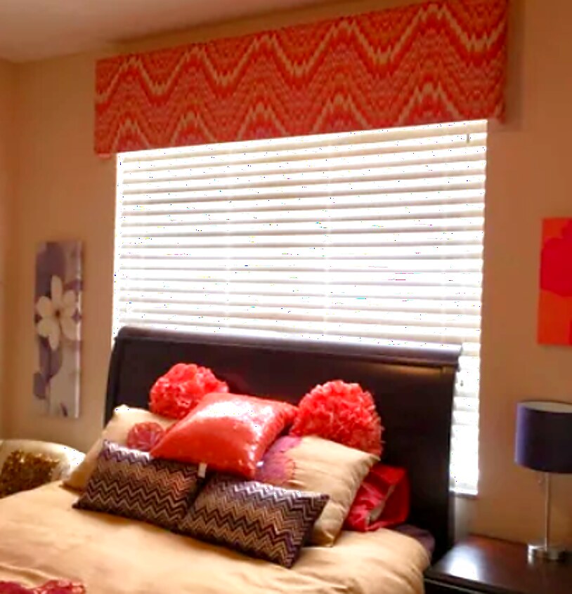 Upholstered cornice in a coral flame-stitch fabric mounted above a bedroom window with white wood blinds