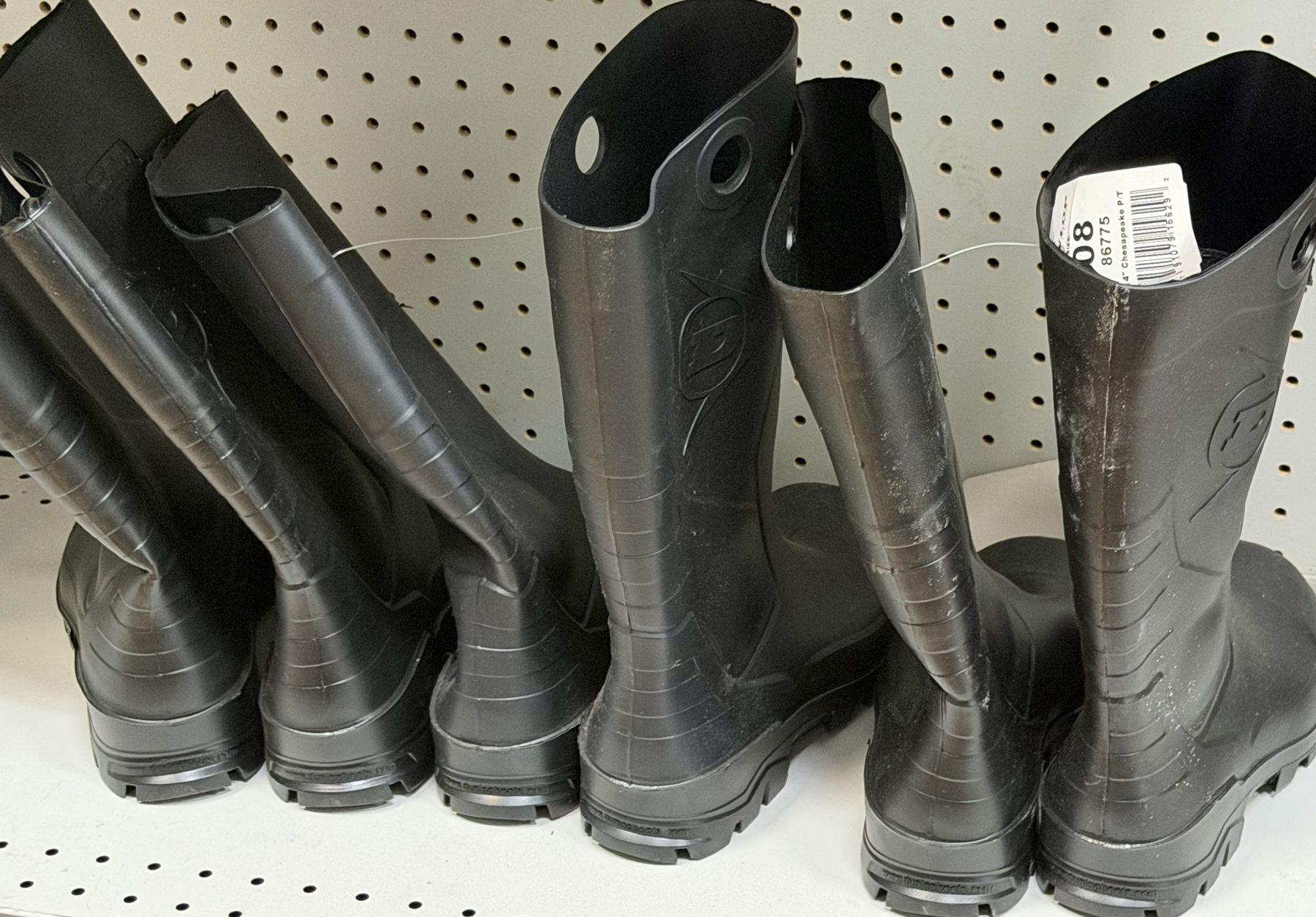 Black Dunlop Chesapeake waterproof rubber work boots displayed on a pegboard shelf at Hessler Paint & Hardware in Delray Beach, Florida.