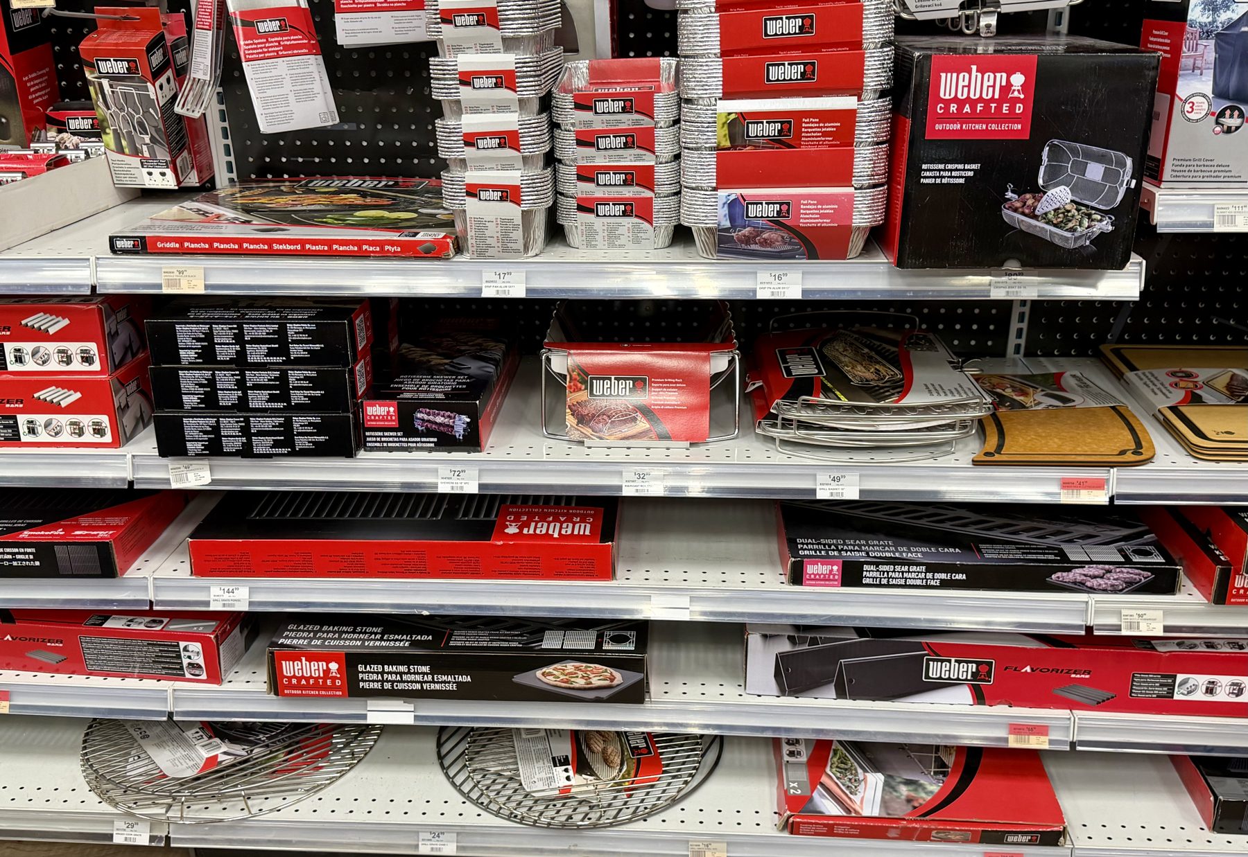 Shelves stocked with Weber grill accessories including Weber Crafted Outdoor Kitchen Collection accessories, foil drip pans, sear grates, glazed baking stones, and griddles at Hessler Paint & Hardware in Delray Beach, Florida.