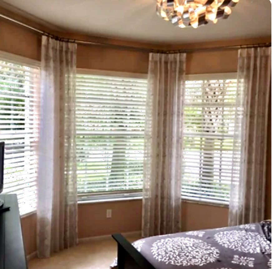 Textured drapery panels on a bedroom bay window layered over white wood blinds