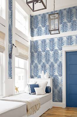 Two-story nook with blue and white printed palm-leaf wallpaper, woven shades, and a window seat