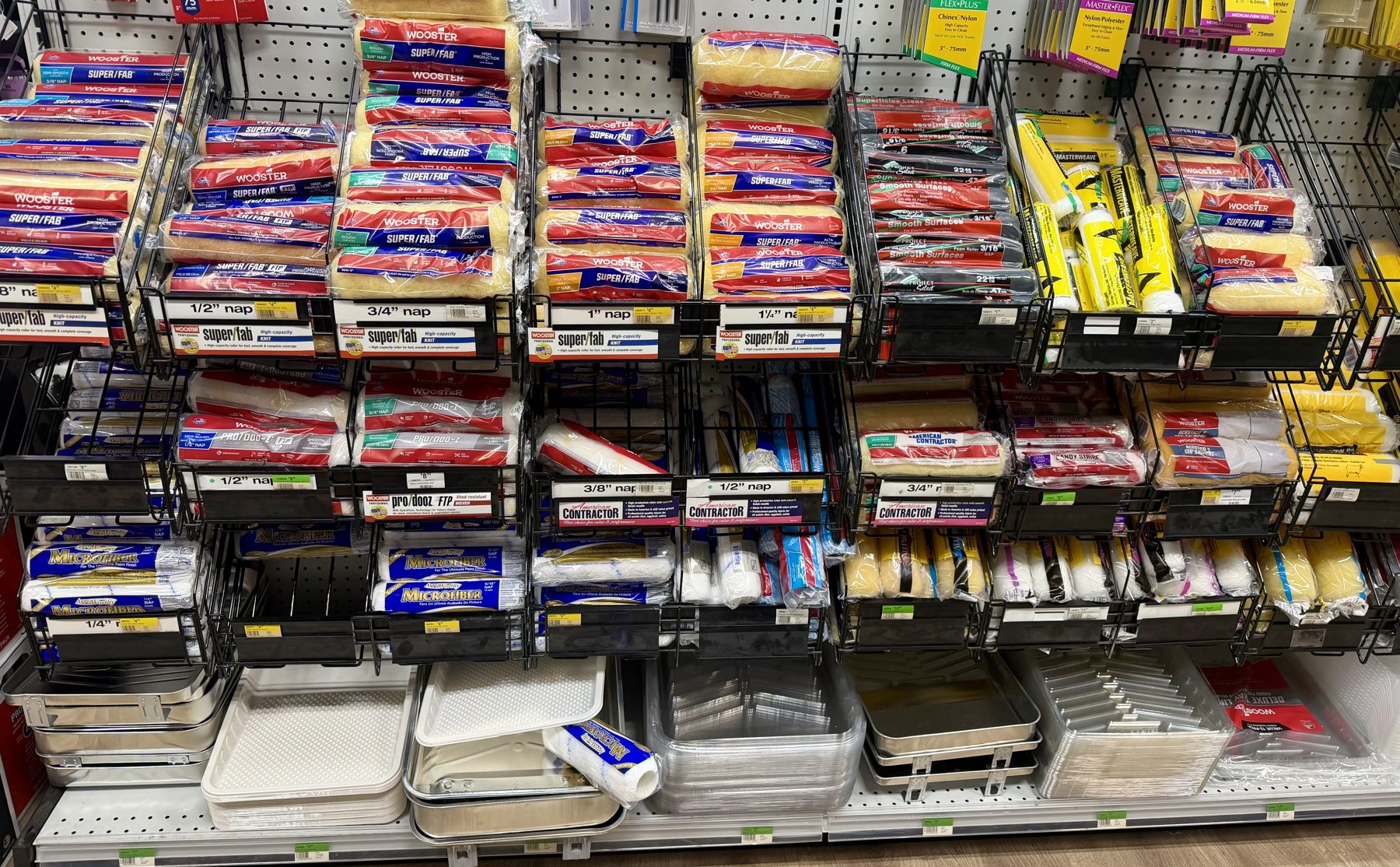 Wall of Wooster paint roller covers sorted by nap size with paint trays and liners at Hessler Paint & Hardware in Delray Beach, Florida.