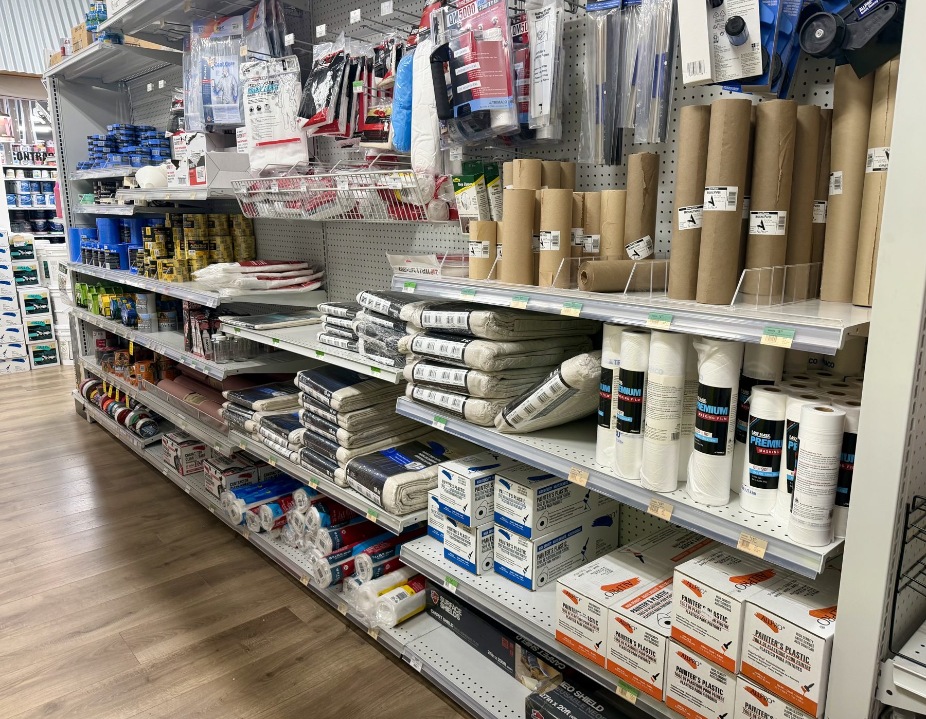 Aisle stocked with canvas drop cloths, masking paper rolls, painter's plastic sheeting, and floor surface protection products at Hessler Paint & Hardware in Delray Beach, Florida.