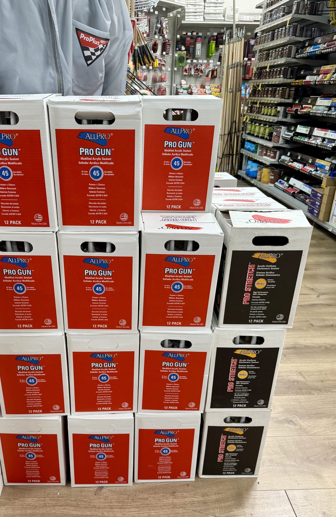 Stacked cases of ALLPRO Pro Gun modified acrylic sealant and Pro Stretch acrylic urethane sealant 12-packs displayed in the paint aisle at Hessler Paint & Hardware in Delray Beach, Florida.