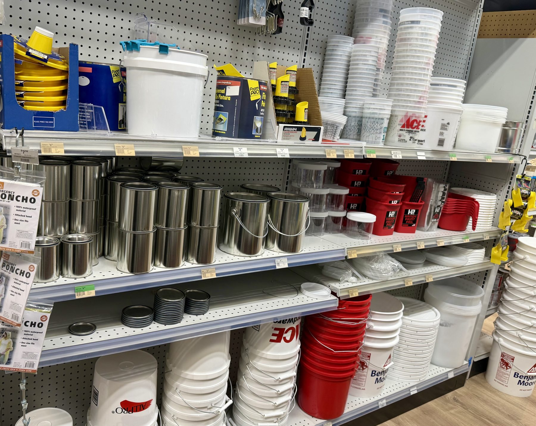 Shelves stocked with empty metal paint cans, plastic paint buckets from Ace Hardware and Benjamin Moore, red Handy Paint Pails, and paint mixing containers at Hessler Paint & Hardware in Delray Beach, Florida.