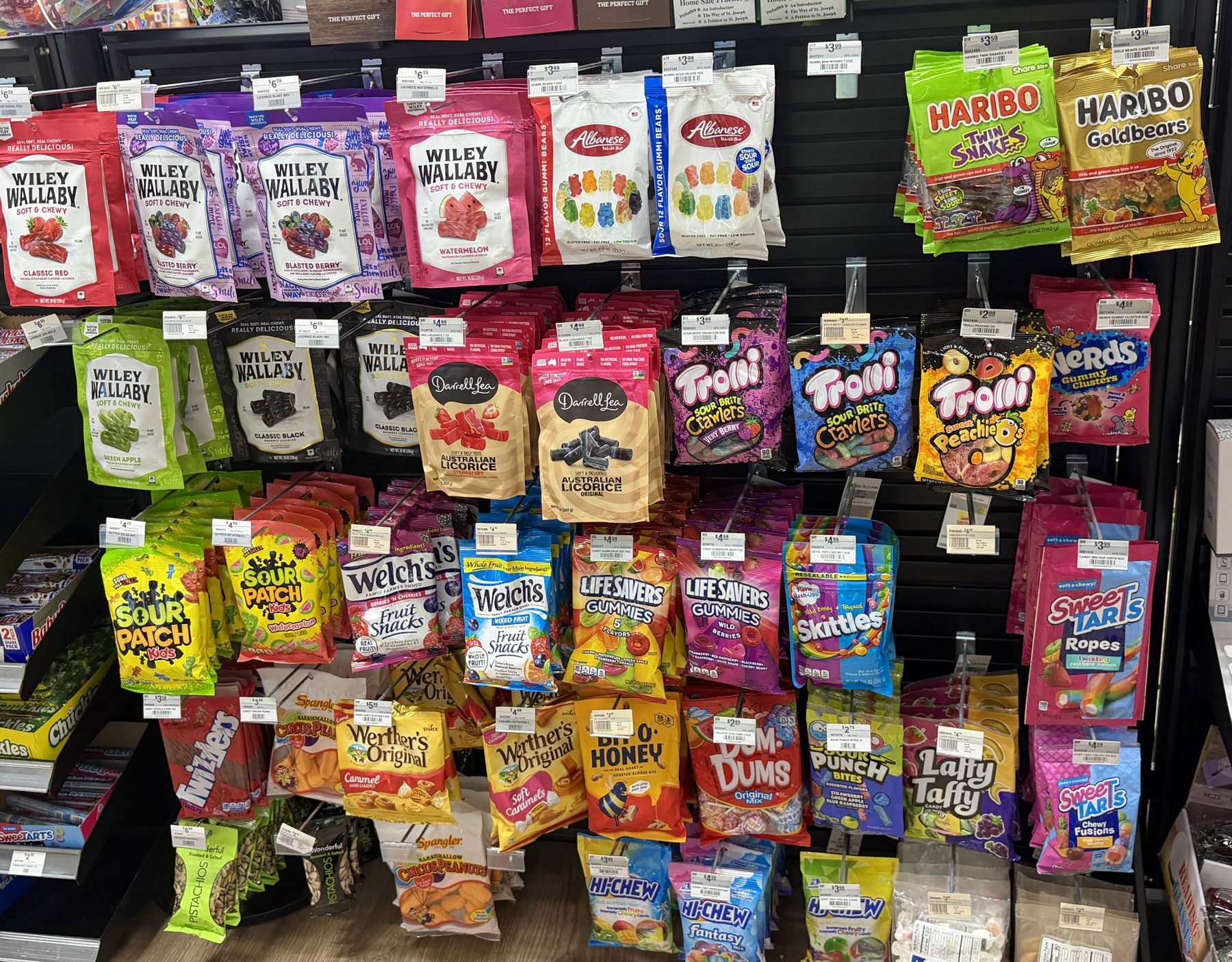 Pegboard display loaded with assorted bagged candies including Wiley Wallaby licorice, Haribo Goldbears, Albanese gummies, Sour Patch Kids, and Werther's Original at Hessler Paint & Hardware in Delray Beach, Florida.