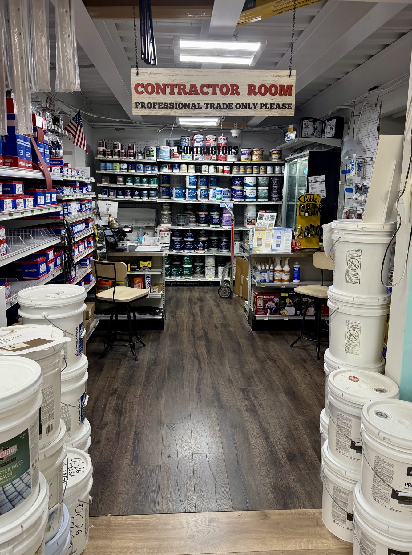 Dedicated contractor room featuring Benjamin Moore paint cans, 5-gallon pails, caulk, and trade service counters at Hessler Paint & Hardware in Delray Beach, Florida.