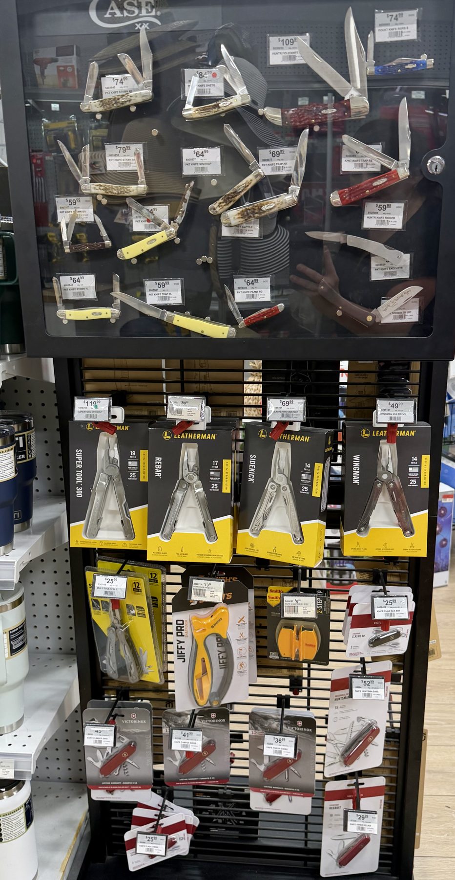 Case XX pocket knives in a glass display case alongside packaged Leatherman multi-tools and Victorinox Swiss Army knives hanging on pegboard at Hessler Paint & Hardware in Delray Beach, Florida.