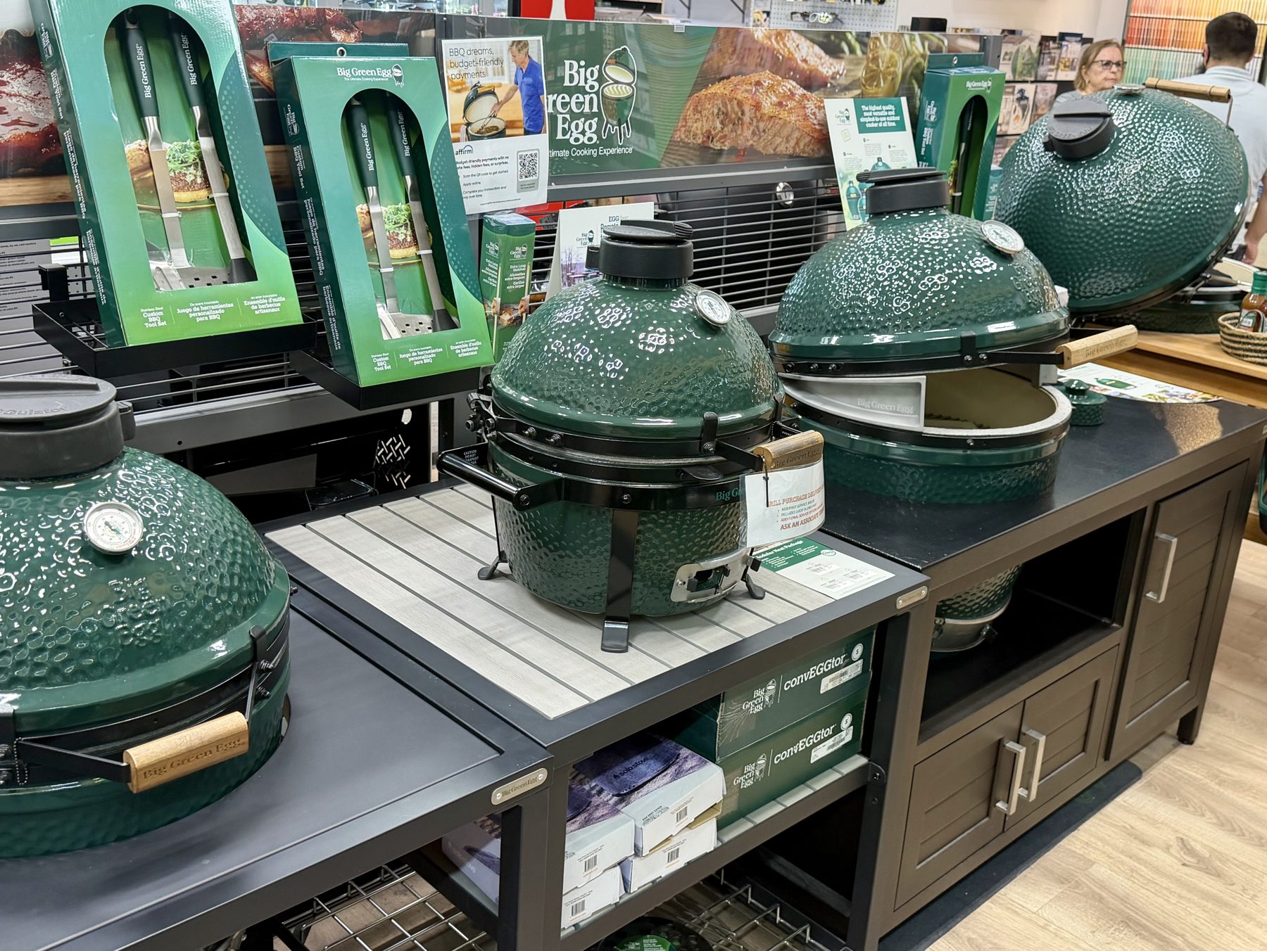 Display of Big Green Egg ceramic kamado grills, packaged barbecue tools, and official accessories on modular outdoor cabinets at Hessler Paint & Hardware in Delray Beach, Florida.