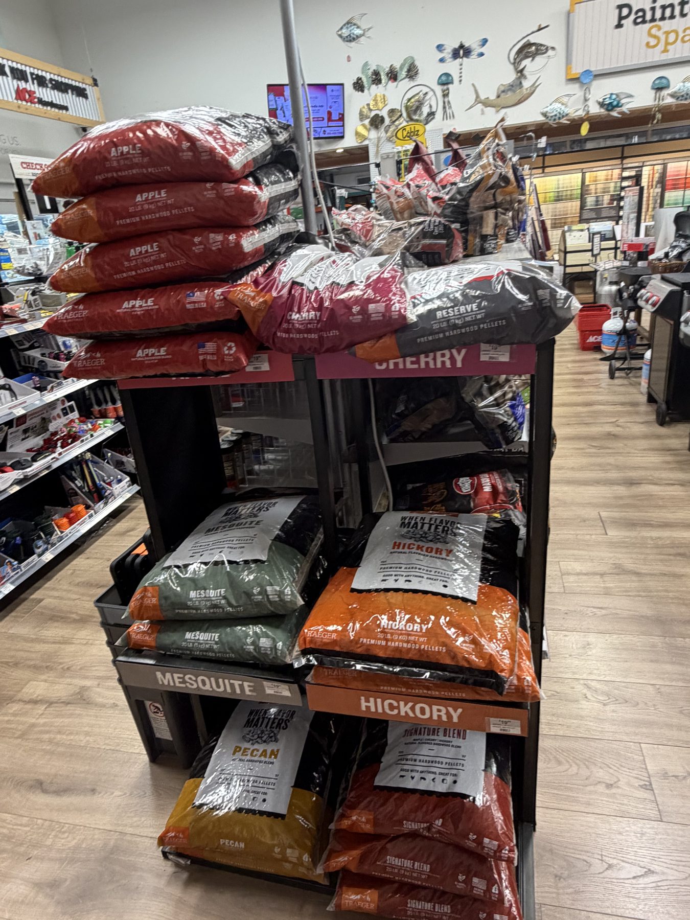 Display shelf stocked with Traeger premium hardwood pellets in flavors like Apple, Cherry, Mesquite, Hickory, and Pecan at Hessler Paint & Hardware in Delray Beach, Florida.