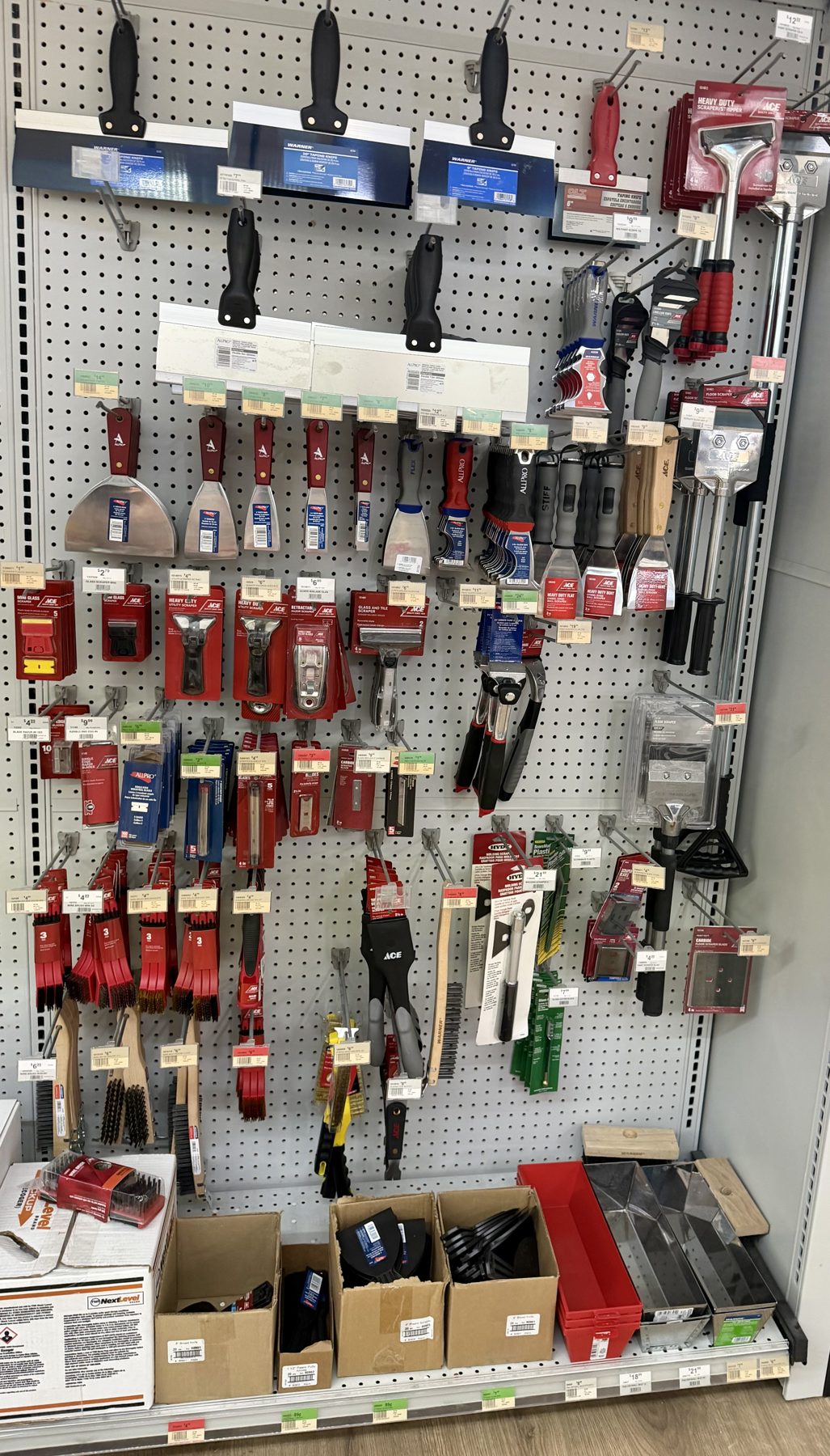 Pegboard display of Ace Brand putty knives, taping knives, scrapers, wire brushes, and drywall mud pans at Hessler Paint & Hardware in Delray Beach, Florida.