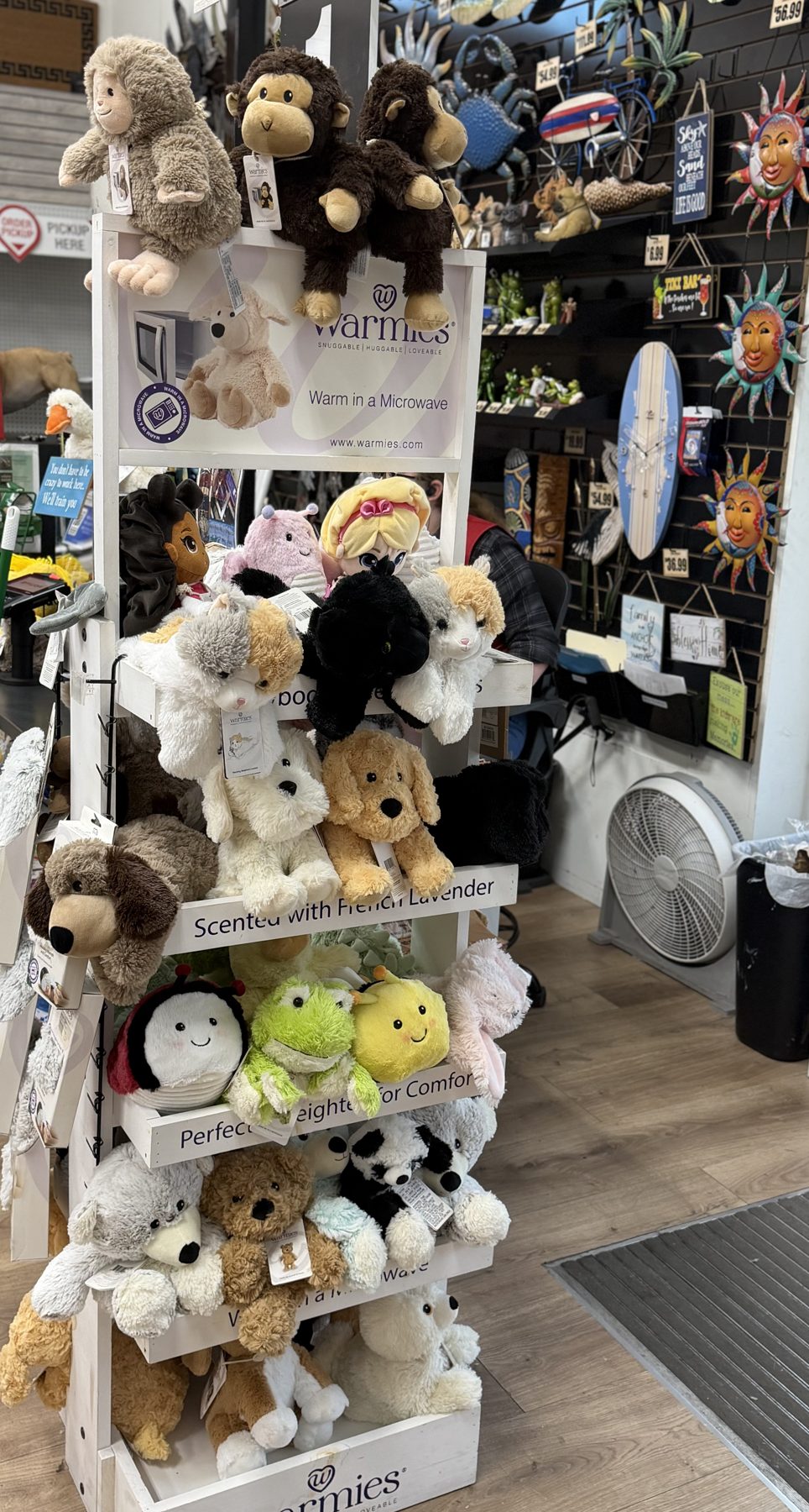 Warmies microwavable lavender-scented plush plushies display stand featuring stuffed animals alongside coastal wall decor at Hessler Paint & Hardware in Delray Beach, Florida.