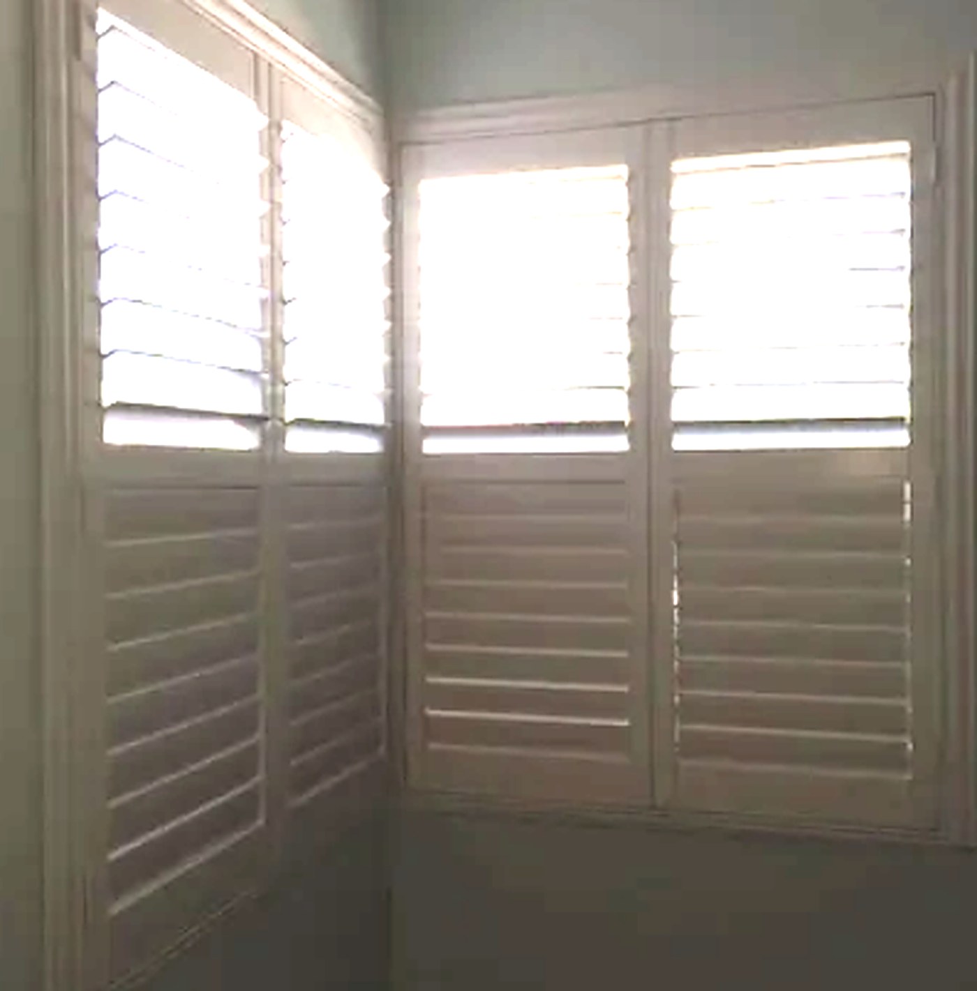 Corner windows with white plantation shutters, lower louvers closed for privacy and upper louvers open for light