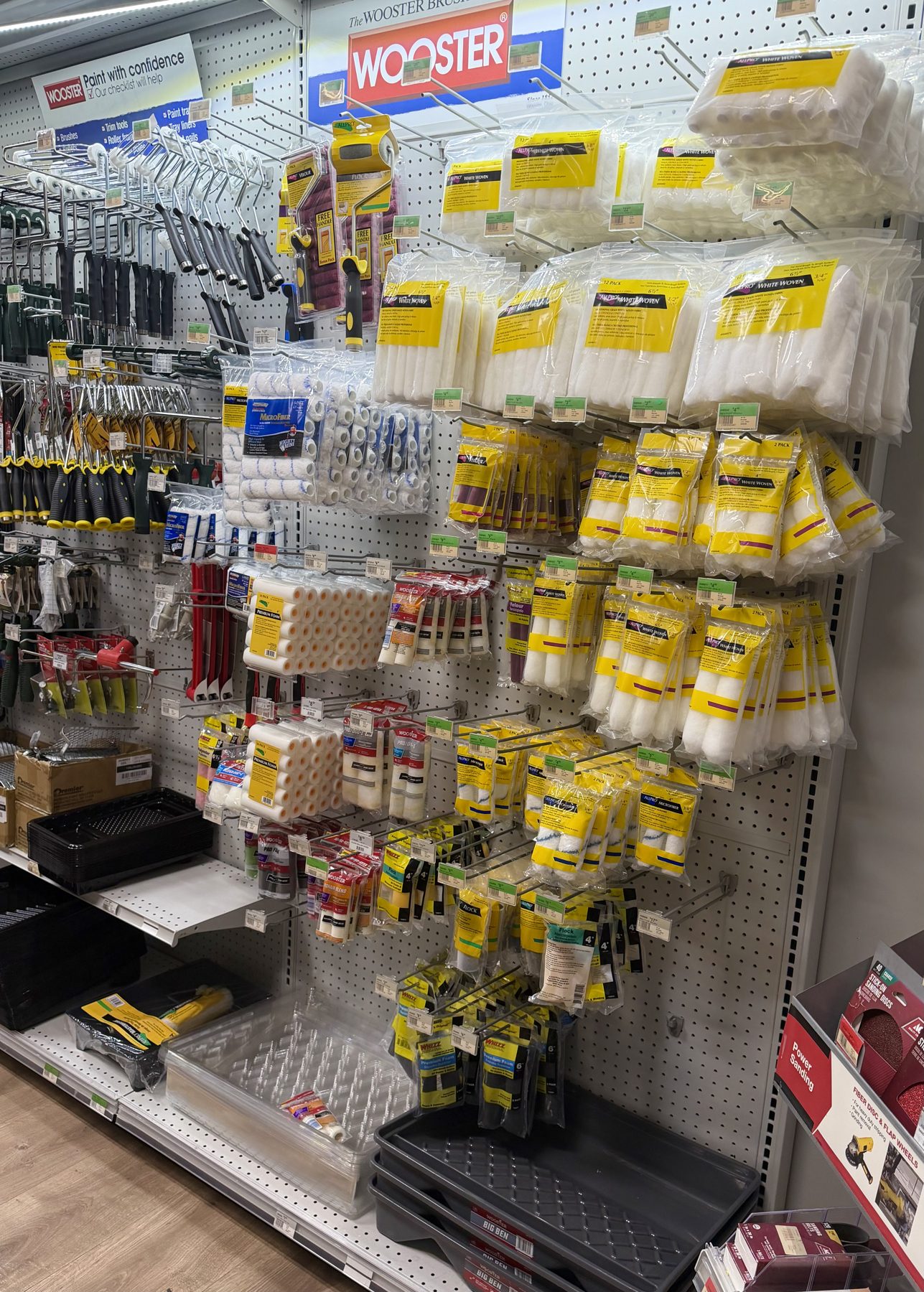 A wide selection of Wooster paint roller covers, roller frames, and paint trays displayed on pegboard walls at Hessler Paint & Hardware in Delray Beach, Florida.