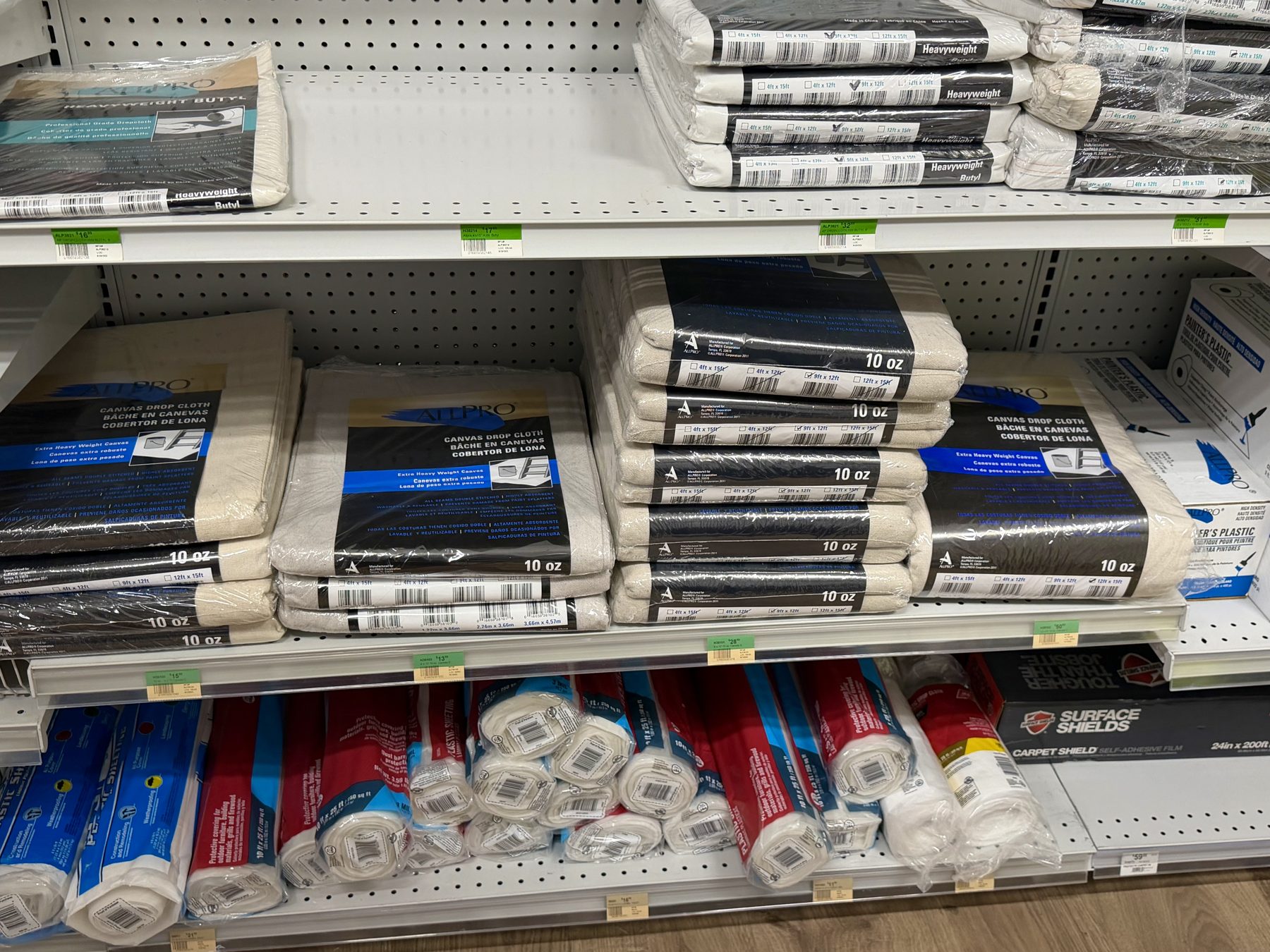 Shelves stocked with ALLPRO 10oz canvas drop cloths, butyl drop cloths, and Surface Shields protective surface films at Hessler Paint & Hardware in Delray Beach, Florida.