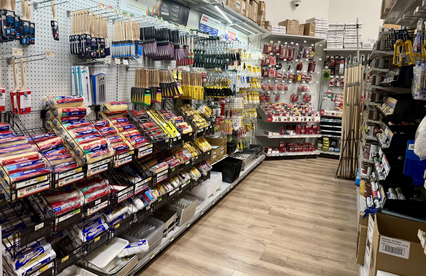 Paint applicators aisle stocked with Wooster roller covers, paintbrushes, paint trays, and extension poles at Hessler Paint & Hardware in Delray Beach, Florida.